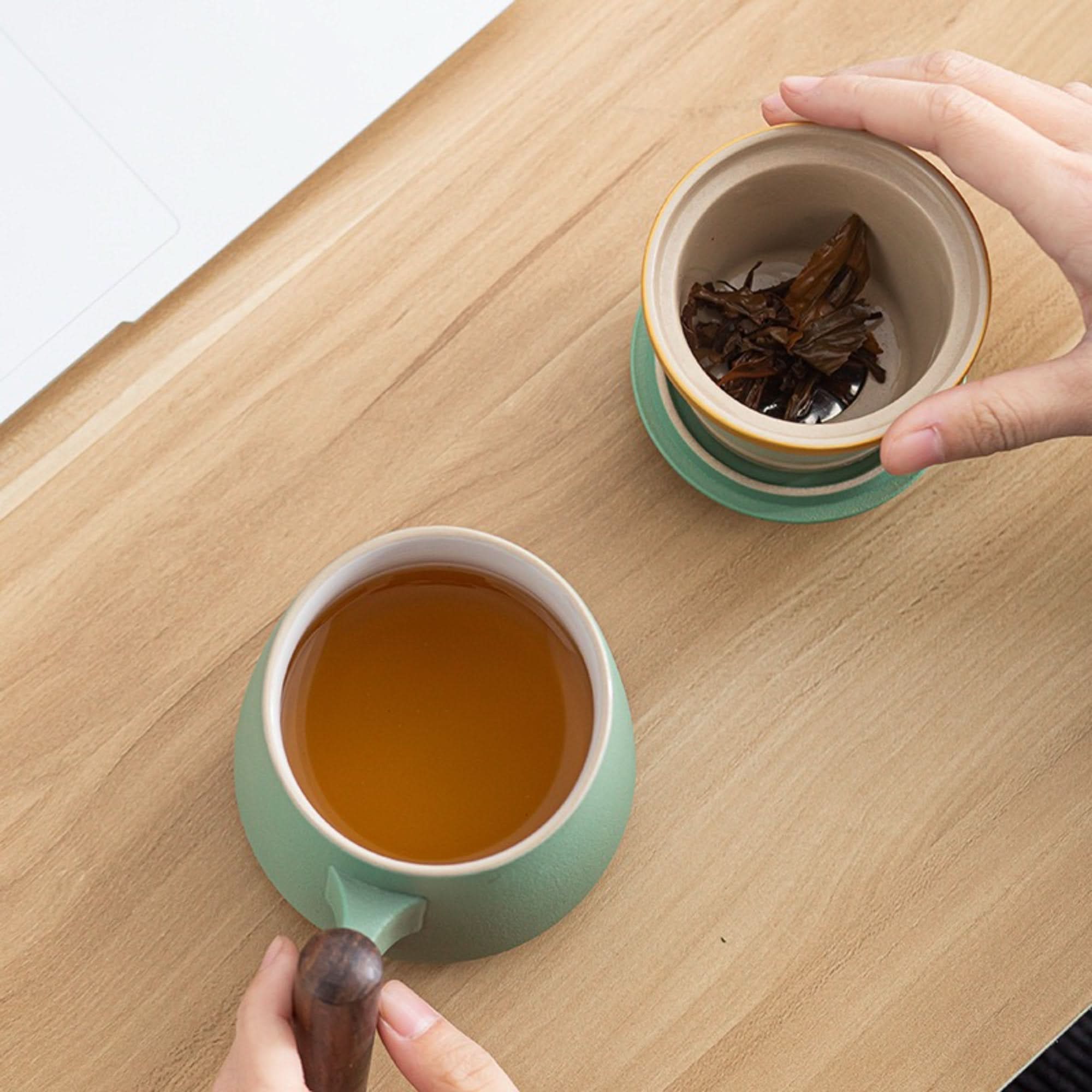 Green Minimalist Japanese Mug with wooden handle filled with amber tea on a wooden desk.
